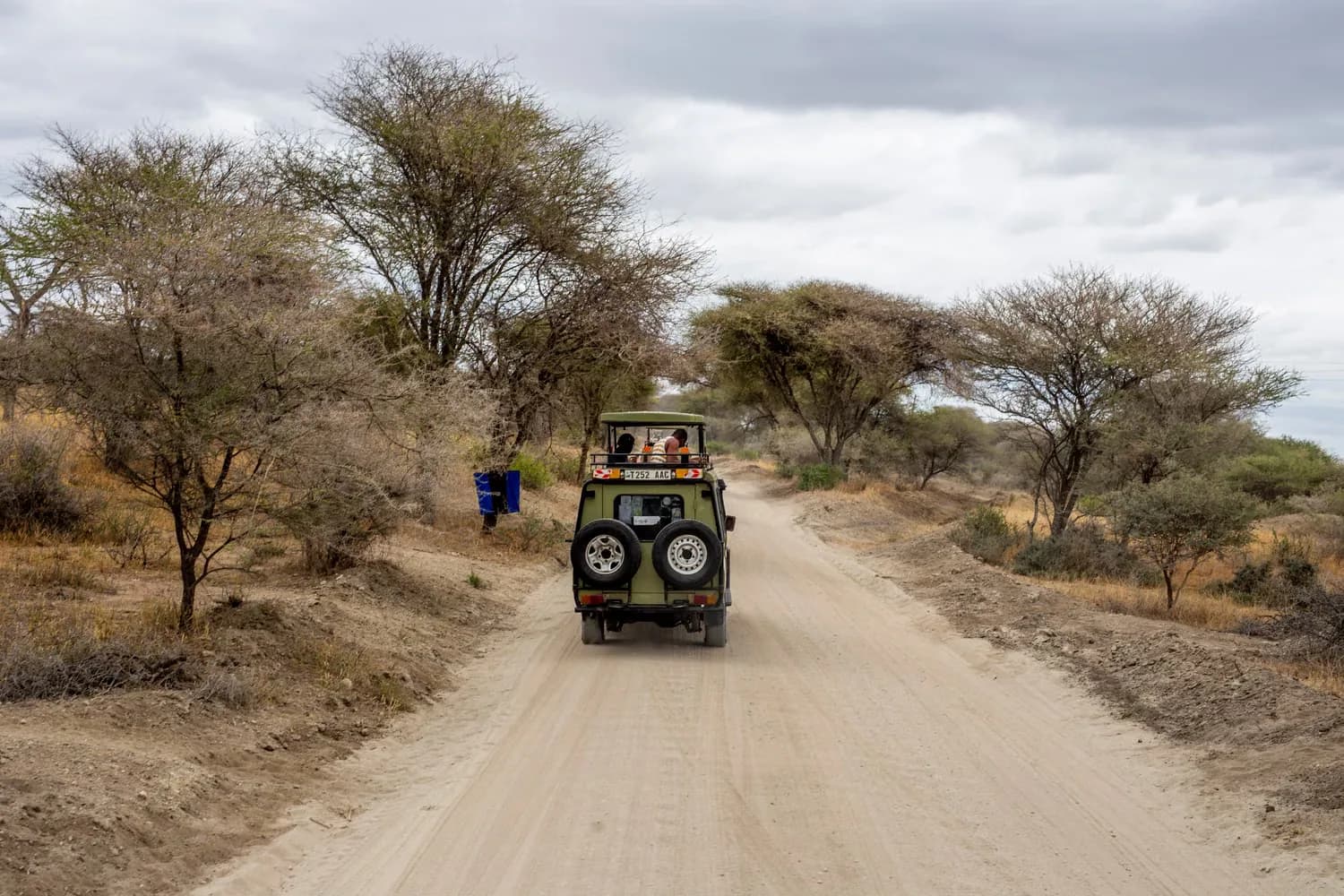 A safari jeep on a dusty dirt road through the African bush